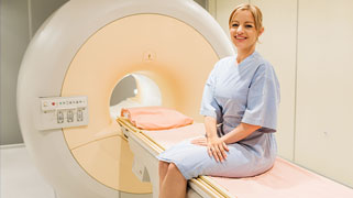 A smiling patient sits on the table of an advanced imaging machine
